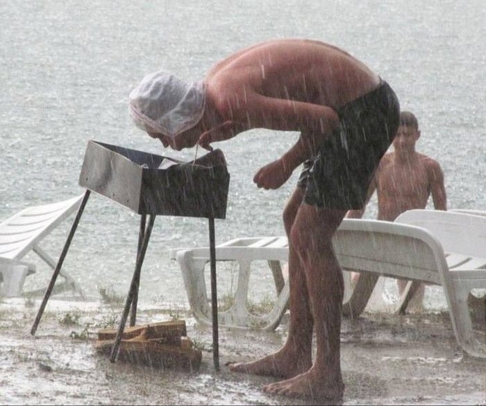Mann versucht bei strömendem Regen den Grill anzufeuern lustig Mann versucht bei strömendem Regen den Grill anzufeuern lustig