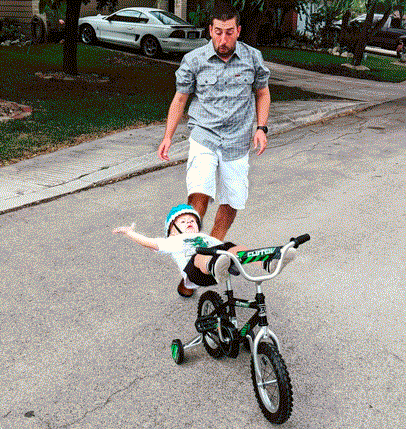 Lustiger Vater bringt Kind Fahrradfahren bei Komische Familienabenteuer und schräge Verwandtschaft Lustiger Vater spielt mit Kind auf Fahrrad - mit dem Sohn Fußballspielen