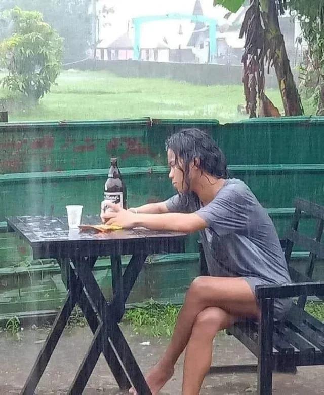 Nachdenklich aussehende Frau genießt ihr Bier bei strömenden Regen.